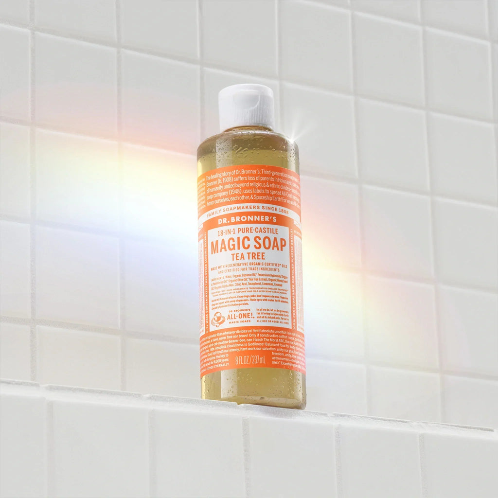A bottle of Dr. Bronners Citrus Pure Castile Soap stands upright on a white tiled surface, illuminated by a soft rainbow light. The setting suggests a bathroom environment [8 oz]