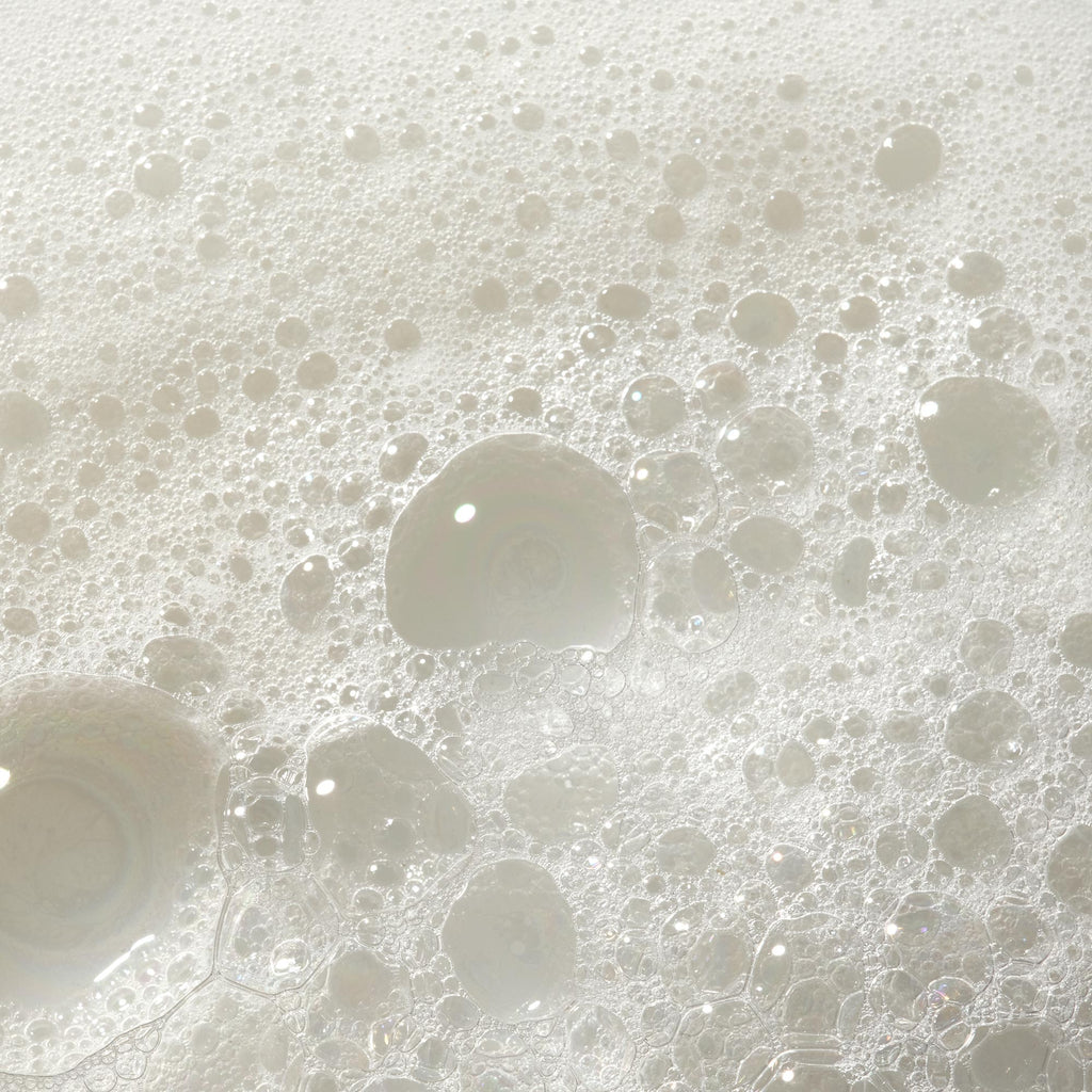 Bubbles form and float on a foamy surface, possibly indicating soap lather. The texture suggests a cleansing action in a bathroom or kitchen setting, showcasing the lightness and purity of the soap [2 oz, 3.4 oz, 4 oz, 8 oz, 16 oz, 32 oz, 1 Gallon]