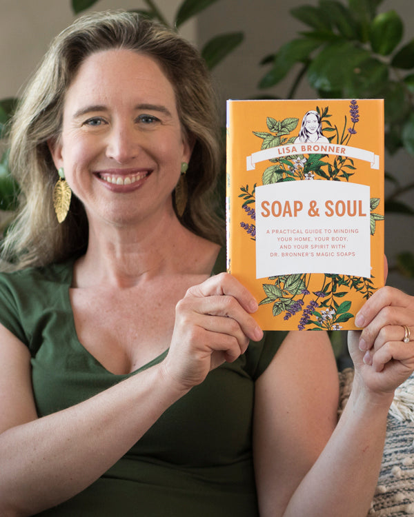 A person smiling holds a book titled Soap Soul with detailed illustrations on the cover. They sit in a cozy indoor setting, suggesting a relaxed reading environment