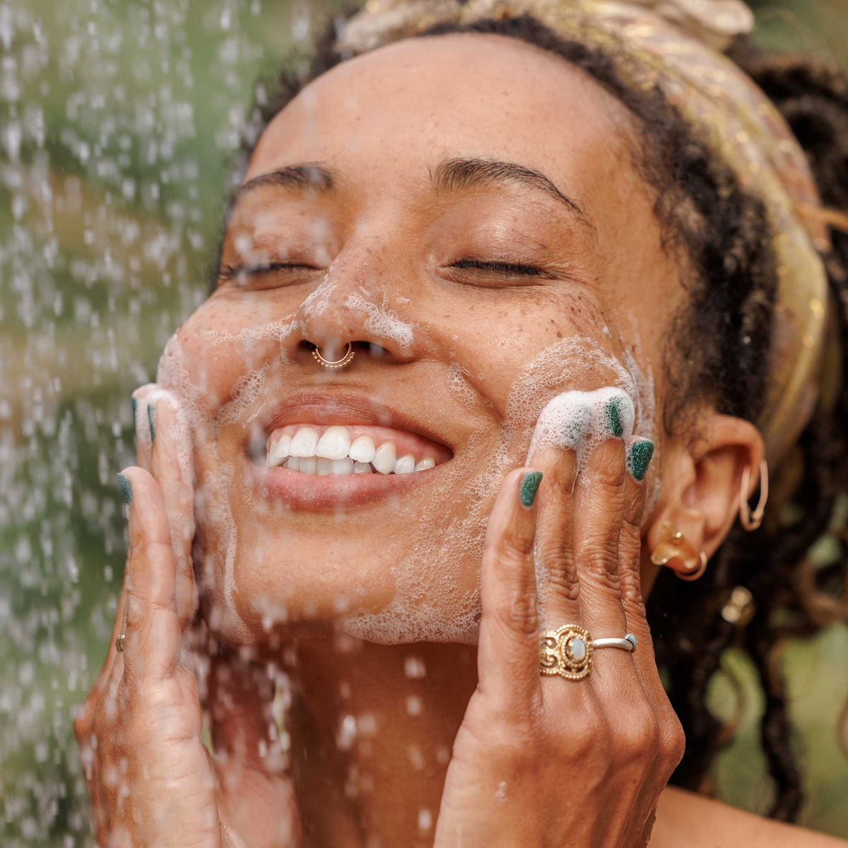 A person joyfully washes their face with soap under a gentle outdoor waterfall, surrounded by lush greenery. The scene evokes a sense of natural, eco friendly cleansing and sustainable living  [2 oz, 3.4 oz, 4 oz, 8 oz, 16 oz, 32 oz, 1/2 Gallon, 1 Gallon]