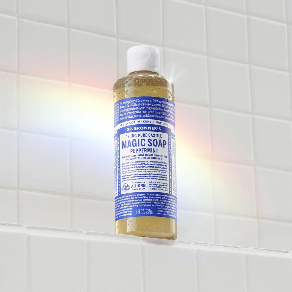 A bottle of Dr. Bronners Pure Castile Liquid Soap, labeled in blue, sits on white tiled backdrop with a rainbow light effect across it. The text reads Dr. Bronners 18 in 1 Hemp Peppermint Pure Castile Soap [8 oz]